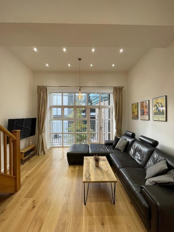 a living room with a black leather couch and a table at Stunning 3BD Maisonette wBalcony - Old Street! in London