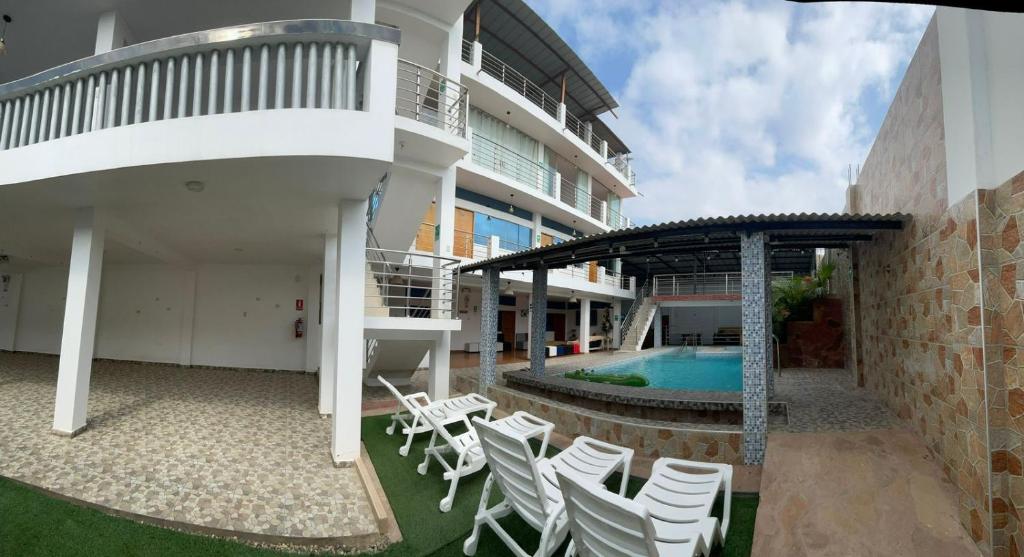 un patio con sillas blancas y una piscina en Hotel Pinos del Mar en Zorritos