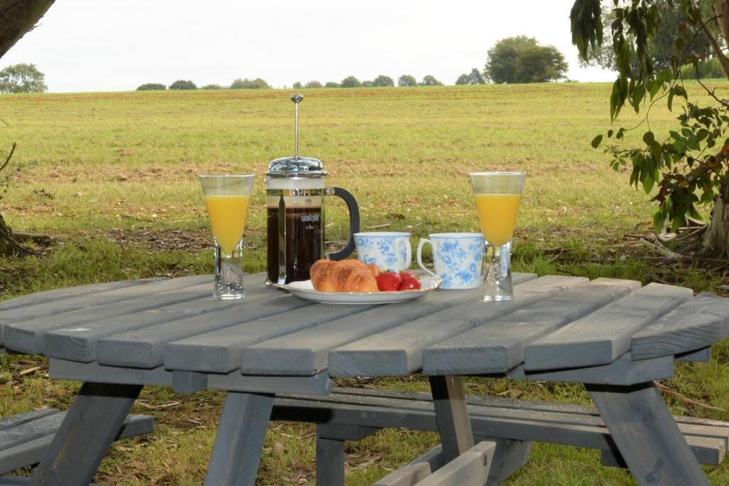 stolik piknikowy z talerzem jedzenia i dwie szklanki soku pomarańczowego w obiekcie Paradise in the Oxfordshire Cotswolds w mieście Epwell