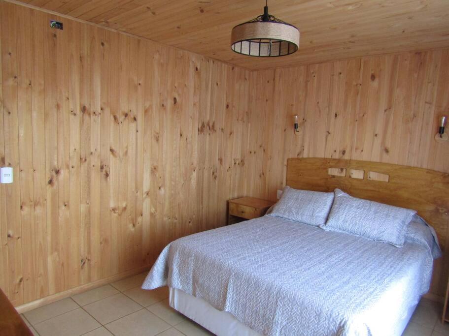 een slaapkamer met een bed en een houten muur bij Comoda Cabaña en Pichilemu in Pichilemu