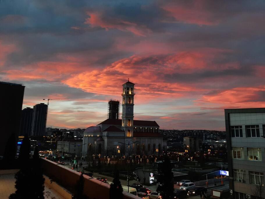 ein Gebäude mit einem Uhrturm in einer Stadt bei Sonnenuntergang in der Unterkunft Prishtina Central Apartment in Pristina