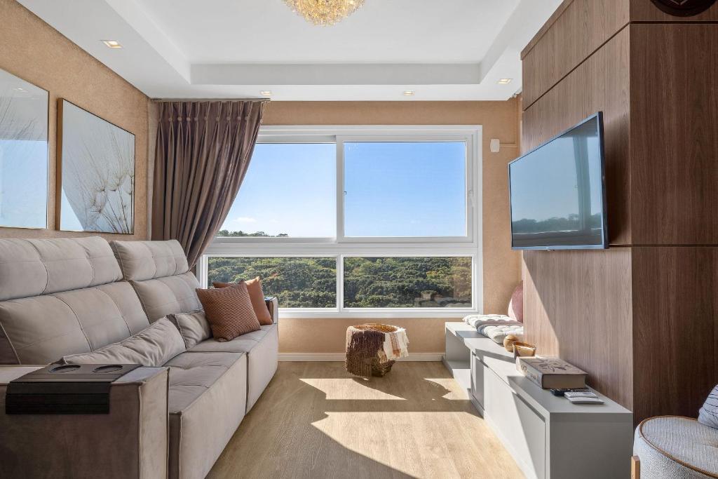 ein Wohnzimmer mit einem Sofa und einem großen Fenster in der Unterkunft Jardins de Gramado 402 B - 3 suítes e linda vista in Gramado