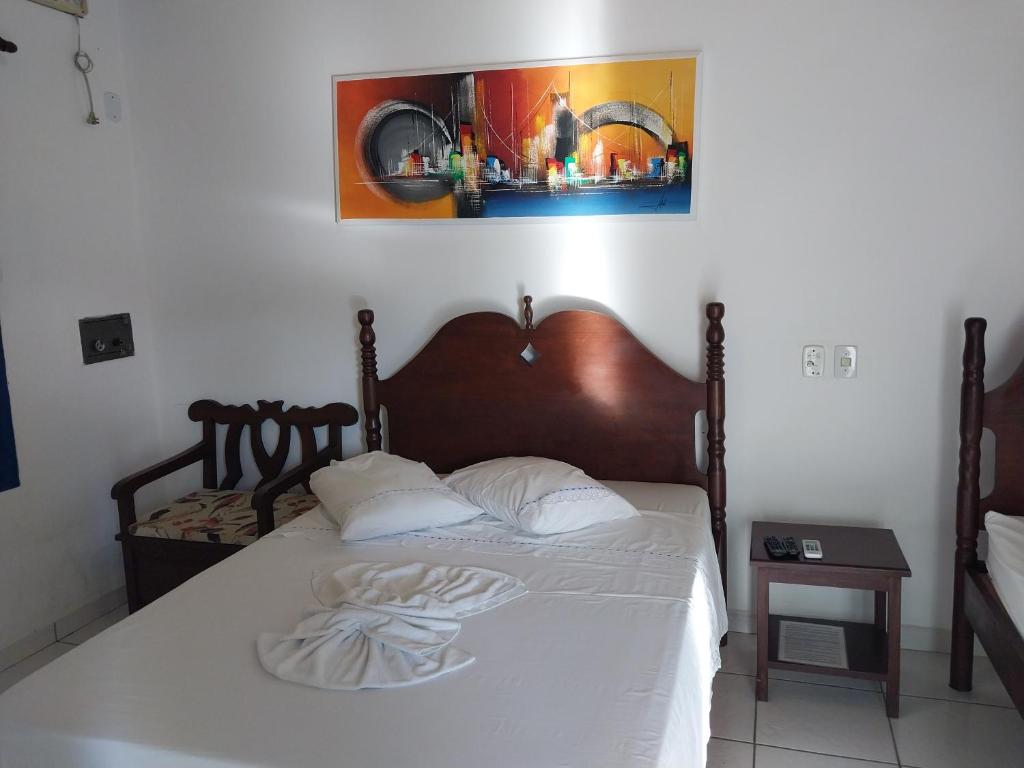 a bedroom with a bed with white sheets and a picture on the wall at Pousada Flores da Terra in Paraty