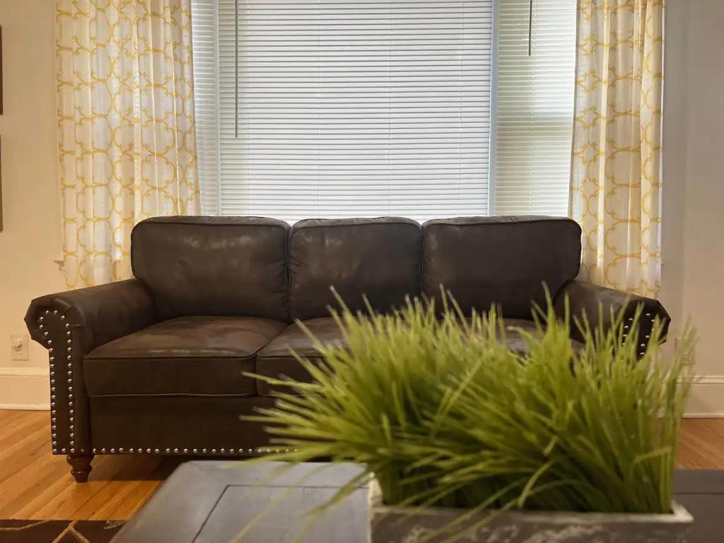 a brown leather couch in a living room with a window at Greensboro Downtown House in Greensboro