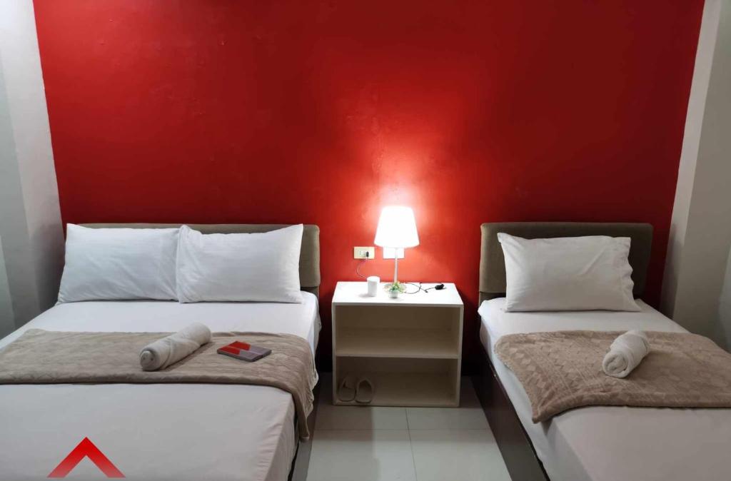 two beds in a room with a red wall at MANTRA PENSIONNE Standard Room in Cagayan de Oro