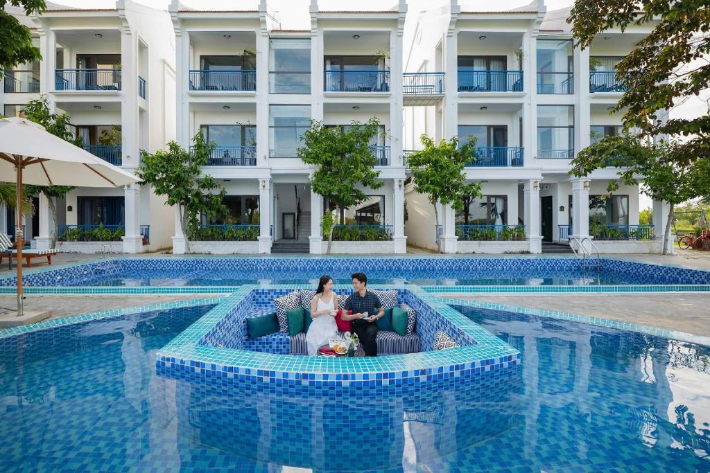 a bride and groom sitting on a couch in front of a swimming pool at Serene Nature Hotel & Spa in Hoi An