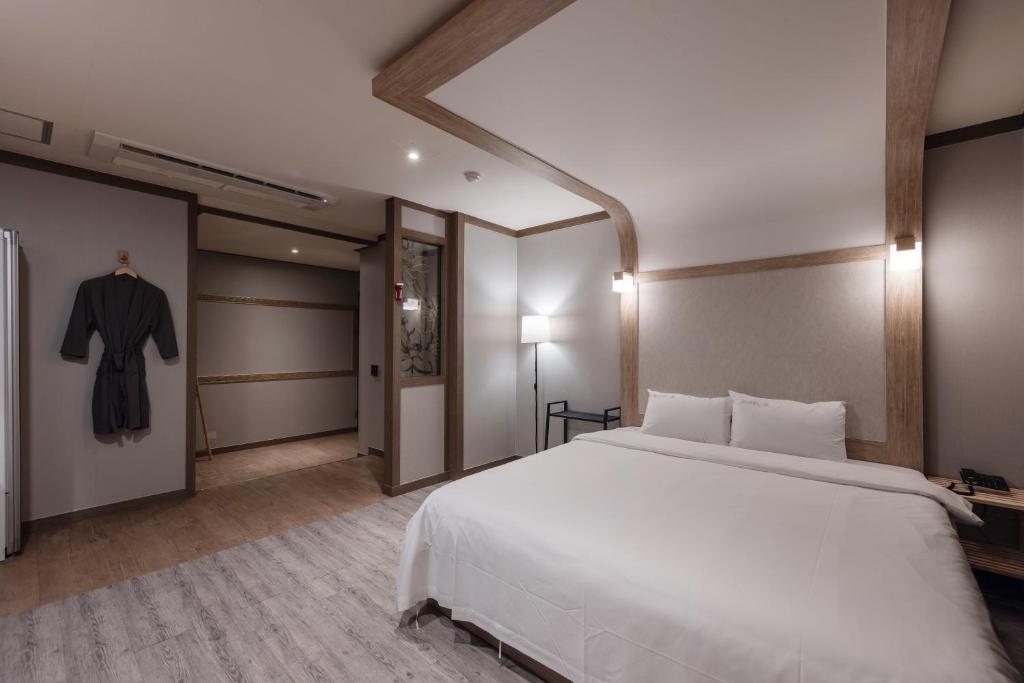 a bedroom with a large white bed and a robe at BELMORE Hotel in Busan