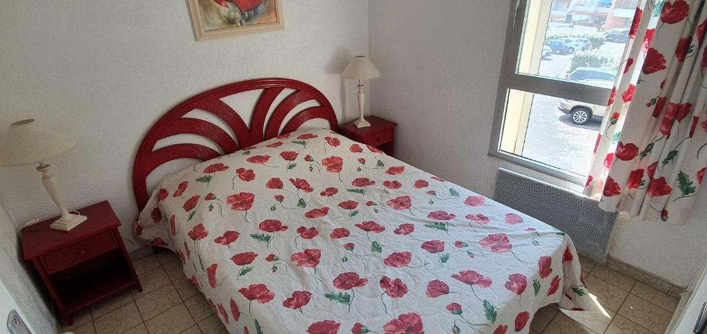 sypialnia z łóżkiem z kwiatową narzutą i oknem w obiekcie 096 Roches Noiires A26 w Cap d'Agde