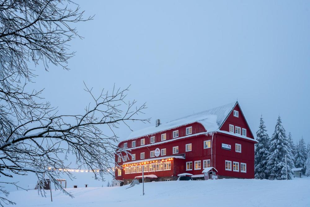 Un grand bâtiment rouge dans la neige avec des lumières de Noël dans l'établissement Prazska Bouda, à Pec pod Sněžkou