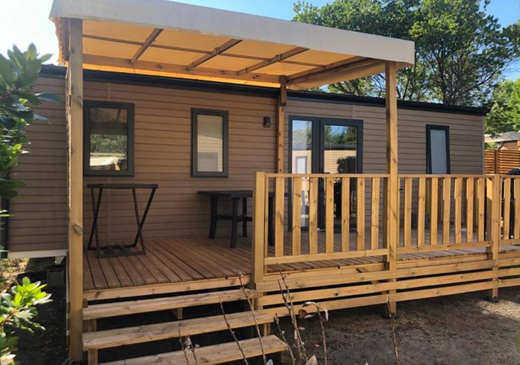 una terraza de madera con toldo en una casa pequeña en Charmant dans camping 5 étoiles-lac en Biscarrosse