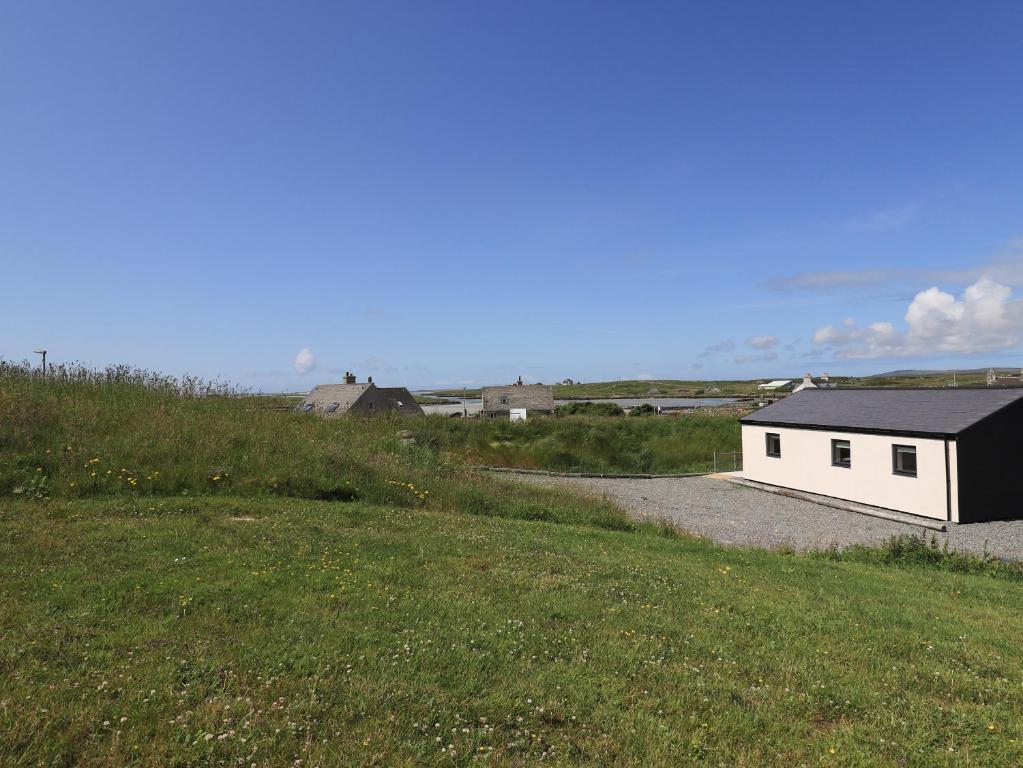 a small white building on a gravel road next to a field at Eala Bhàn Cottage in Carinish