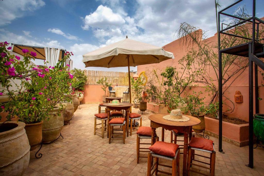 eine Terrasse mit Tischen, Stühlen und einem Sonnenschirm in der Unterkunft Riad Dabachi in Marrakesch