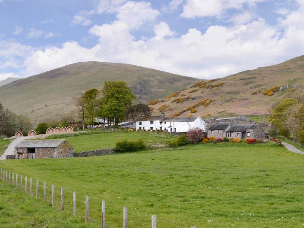 a farm in a field with a hill in the background at Lowside Farm Glamping in Troutbeck