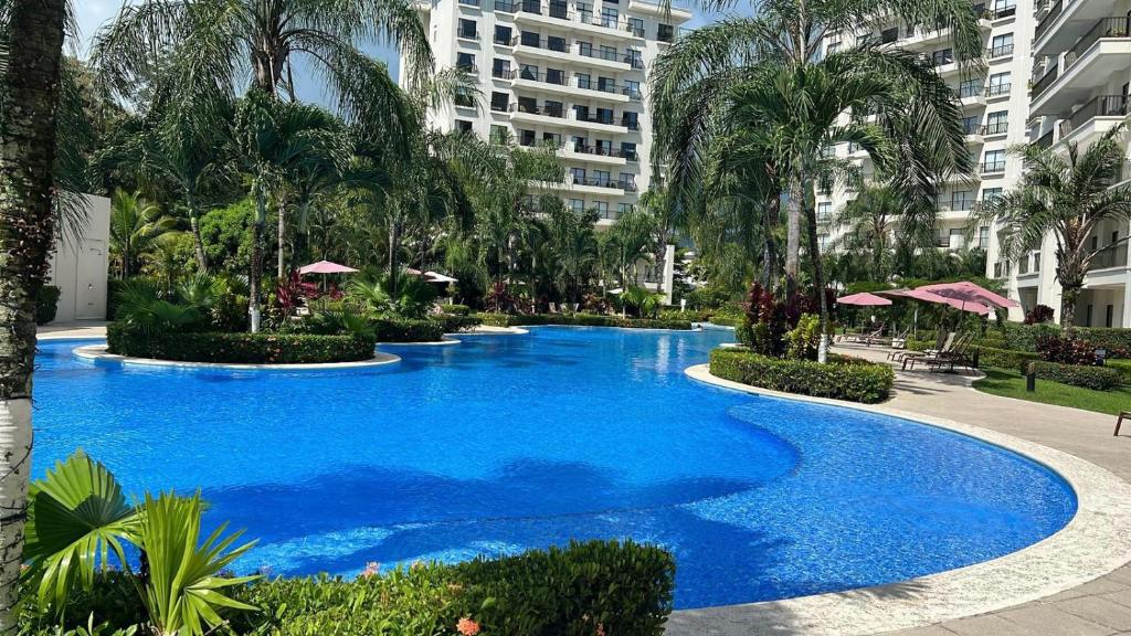 a large blue swimming pool with palm trees and buildings at Private Modern Condo by Jac Beach in Jacó