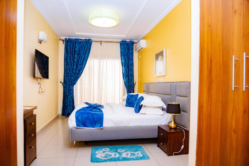 a bedroom with a bed and a window with blue curtains at Loumia Premium Bonapriso in Douala