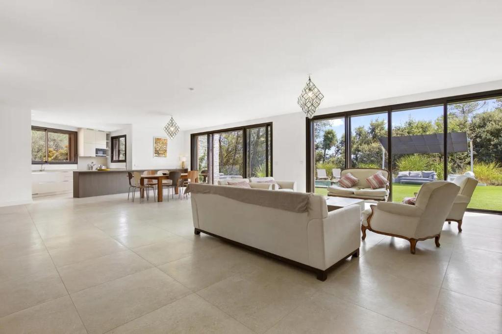 Elle comprend un salon doté d'un mobilier blanc et de grandes fenêtres. dans l'établissement Rez de Villa Valeriane, à Trans-en-Provence