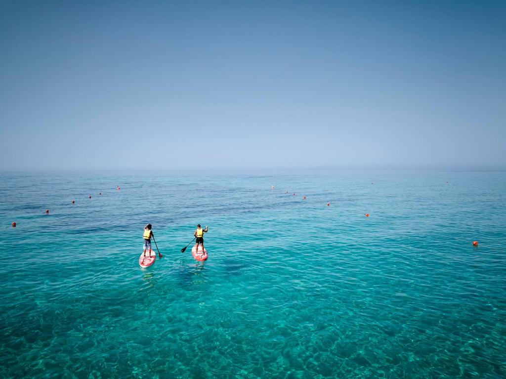 two people are on paddle boards in the ocean at Calaserena Resort in Geremèas