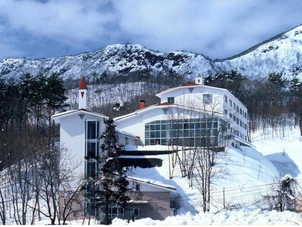 a large white building in the snow with a mountain at Hotel Oakhill in Zaō Onsen