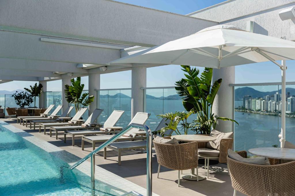 einen Pool mit Stühlen, Tischen und einem Sonnenschirm in der Unterkunft LK Design Hotel Florianópolis in Florianópolis