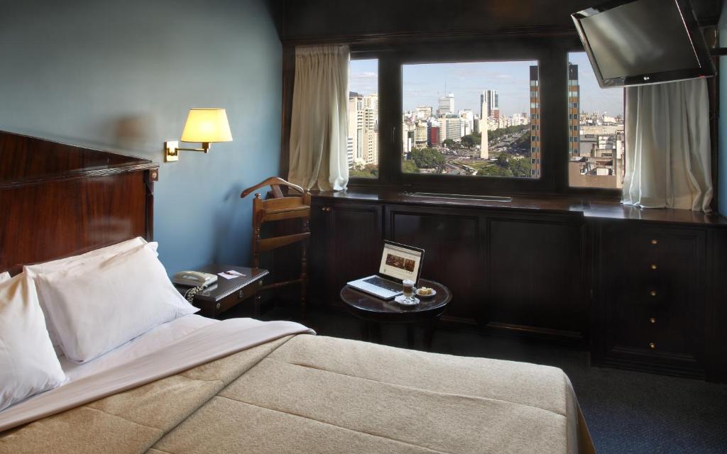 a bedroom with a bed and a window with a laptop on a table at Hotel Presidente Buenos Aires in Buenos Aires
