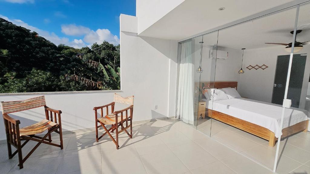 a bedroom with a bed and two chairs on a balcony at Estúdio Arruda in Itacaré