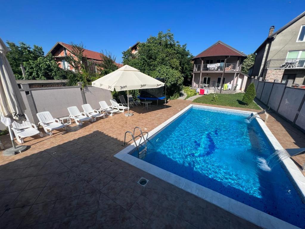 a swimming pool with chairs and an umbrella at Apartman Ms in Jajinci