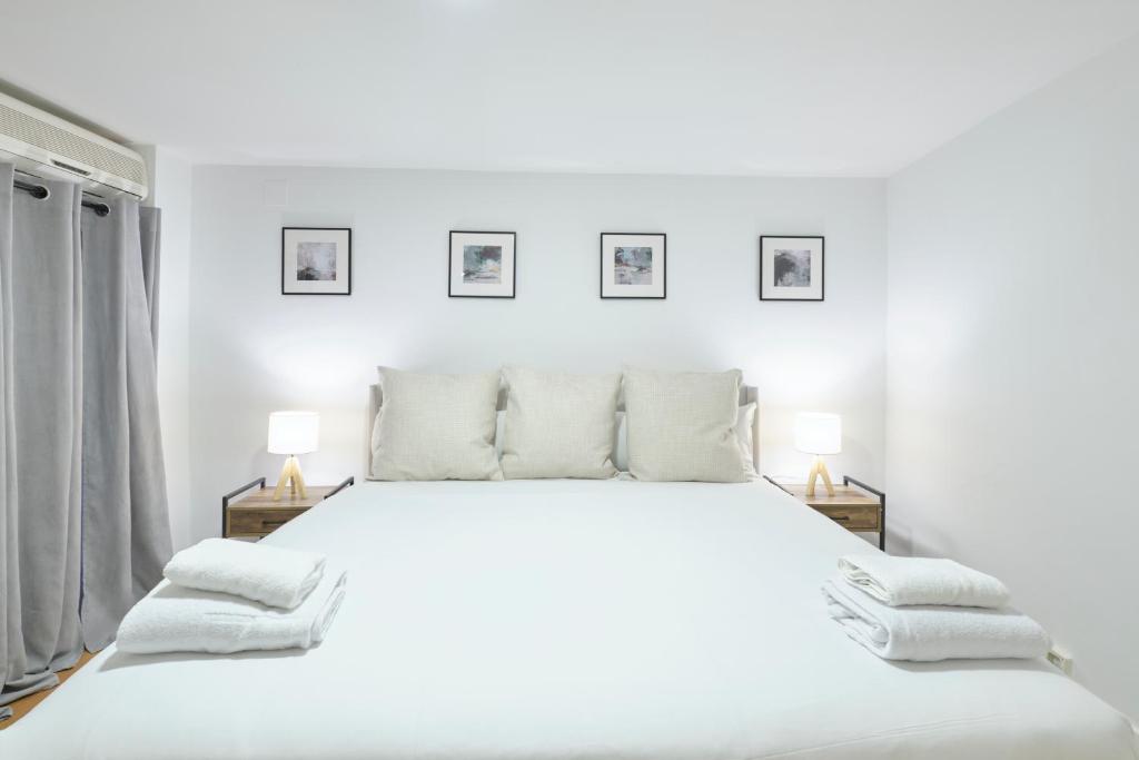 ein weißes Schlafzimmer mit einem großen weißen Bett mit zwei Lampen in der Unterkunft Lovely Apartments - Alójate en el corazón de Madrid in Madrid