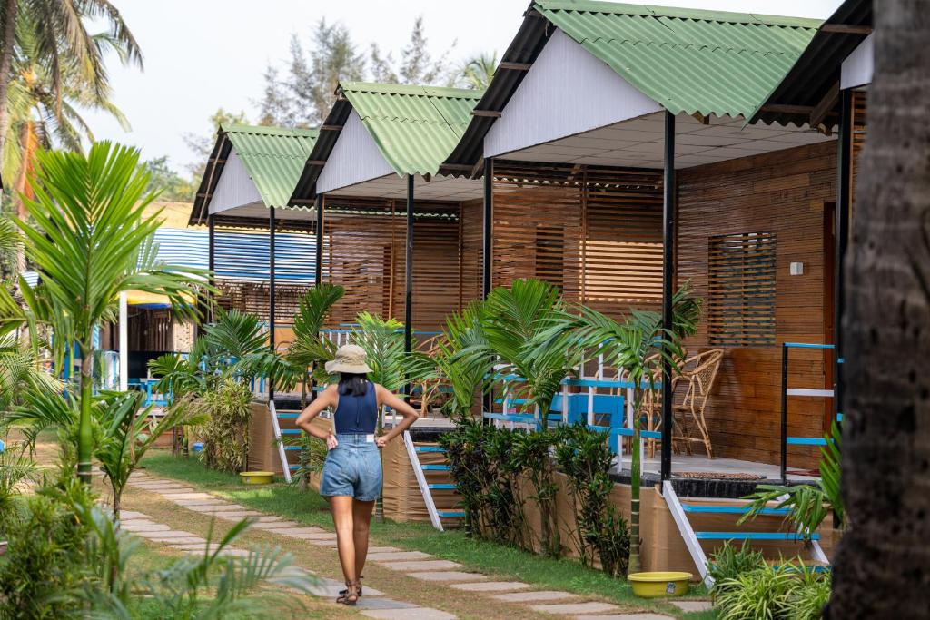 a woman walking down a path in front of a resort at The Tito's Blue Sky Beach resort in Agonda