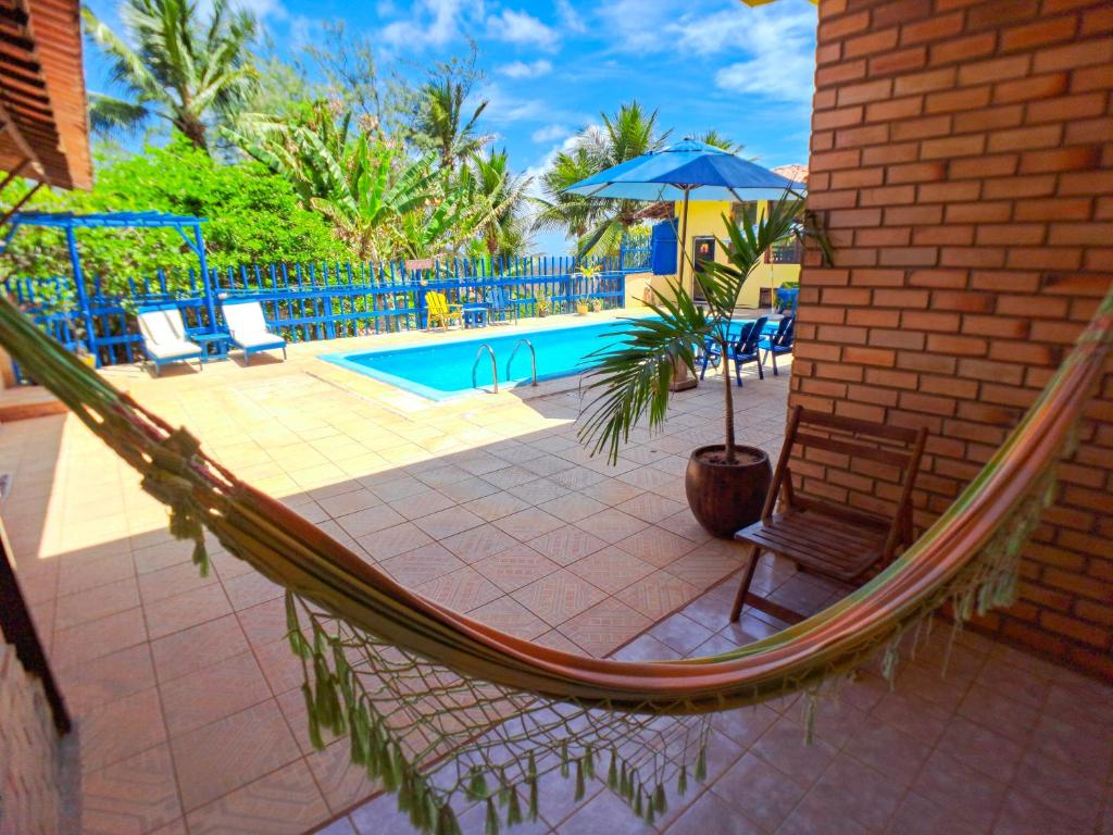 a hammock by a pool with a chair and an umbrella at Pousada Praia do Amor Pipa in Pipa