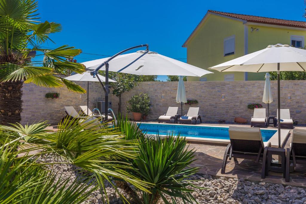 a pool with chairs and umbrellas next to a house at Guest House Antonella in Malinska
