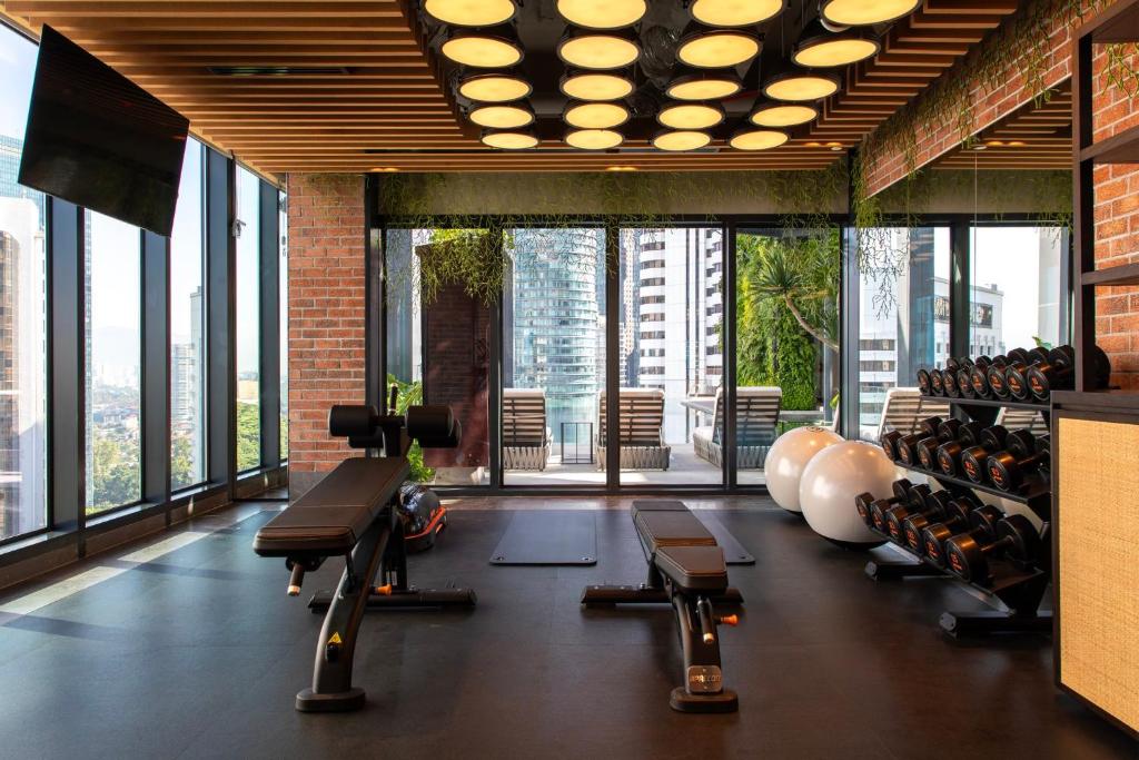 A bright hotel gym has free weights, benches, cable equipment and large windows overlooking the city.