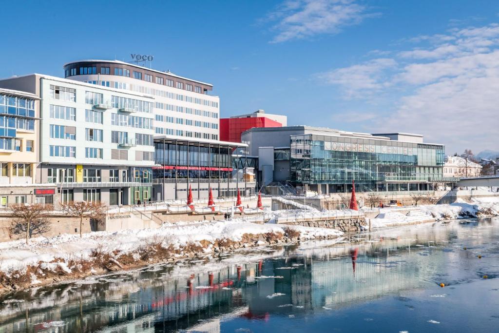 eine Stadt mit Gebäuden und einem Fluss mit Schnee in der Unterkunft voco® Villach, an IHG Hotel in Villach