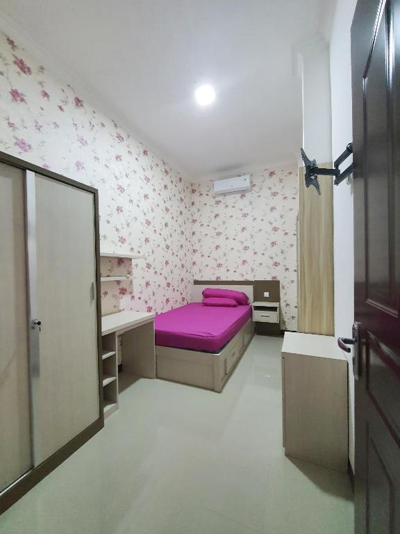 Schlafzimmer mit einem lila Bett und einem Schreibtisch in der Unterkunft Kos Harian Wisma Selma Garuda in Kejayan