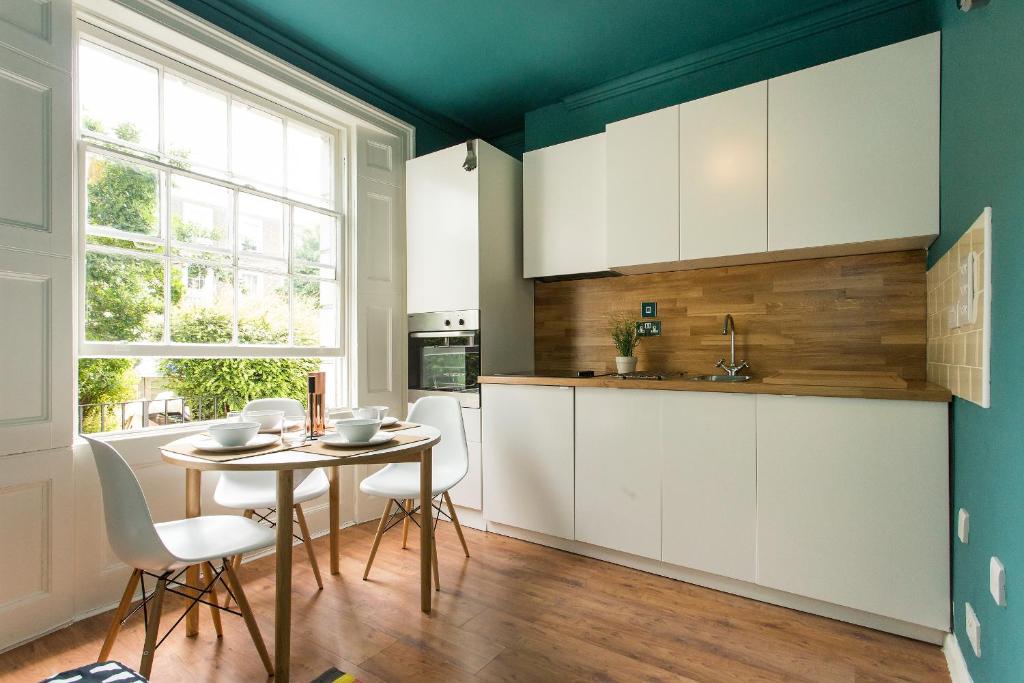 a kitchen with white cabinets and a table and chairs at Camden Apartment By Morethanstays in London