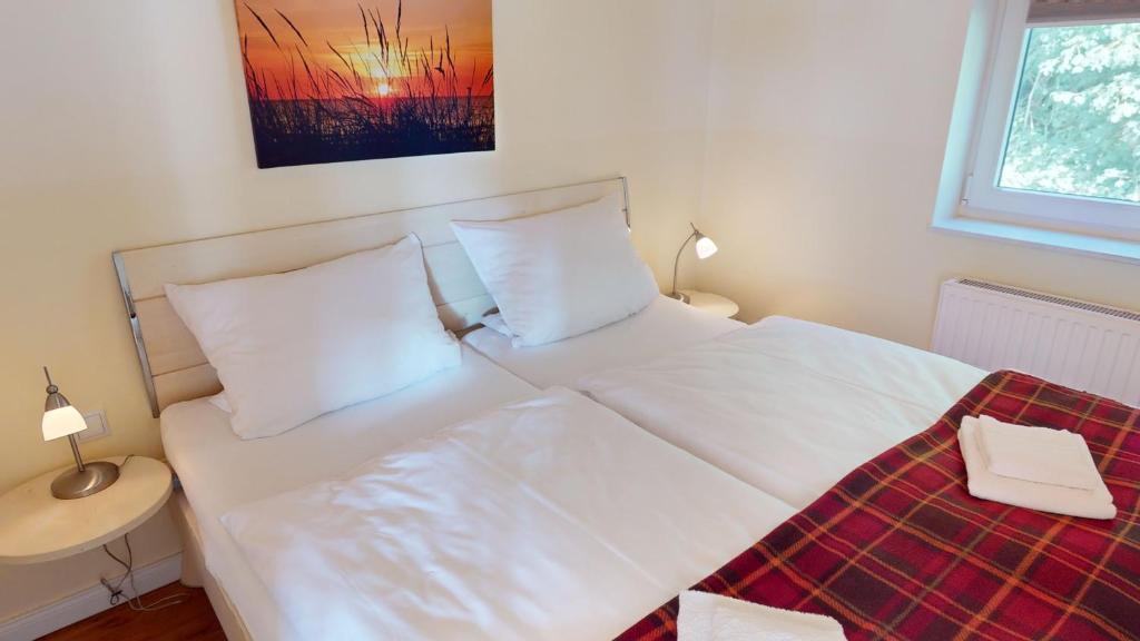 ein Bett mit weißer Bettwäsche und Kissen in einem Schlafzimmer in der Unterkunft Feriendorf Südstrand Haus 22 in Pelzerhaken