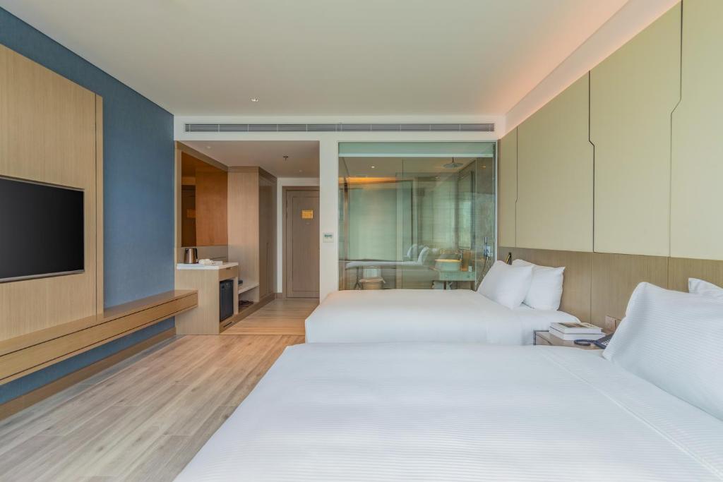 A twin room with two white beds, a television and a fully glazed bathroom partition.