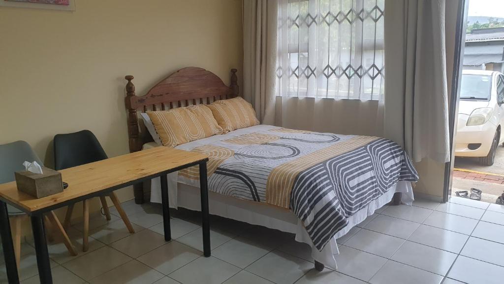 1 dormitorio con cama, mesa y ventana en Manzini, Park Vills Apartment, No 103, en Manzini