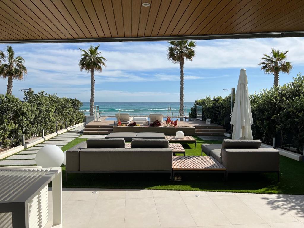 a patio with couches and palm trees and the ocean at Bungalow de lujo 5* 1ª LÍNEA Playa San Juan in Alicante