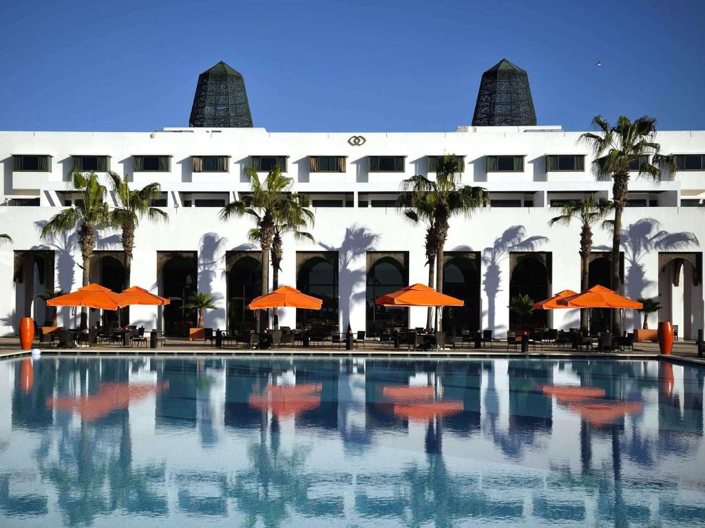 Sofitel Agadir Royal Bay Resort في أغادير: مسبح مع مظلات برتقال امام المبنى