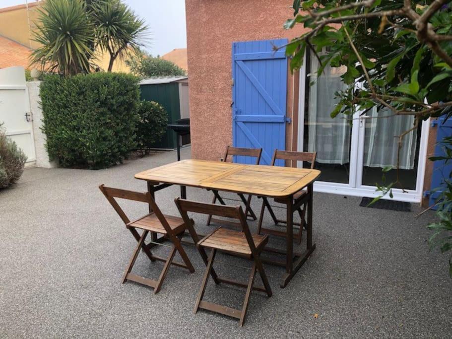 einem Holztisch mit vier Stühlen und einer blauen Tür in der Unterkunft Villa vacances N°23 à 100 mètres de la plage in Saint-Cyprien