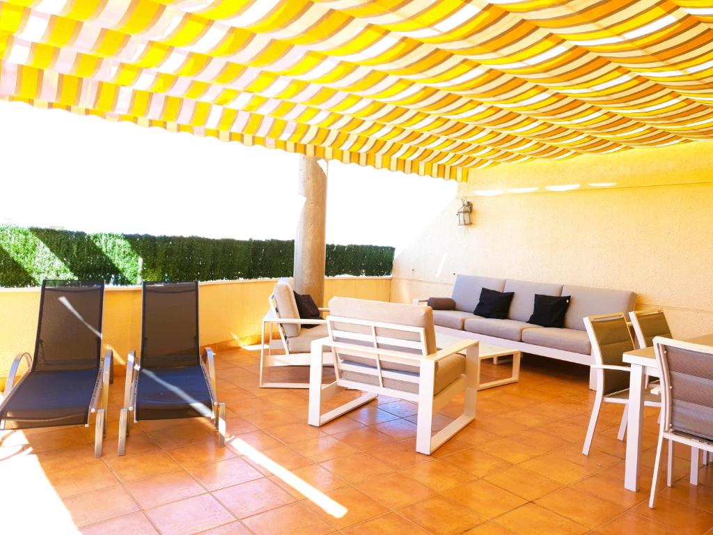 un patio con sillas y un sofá bajo un techo amarillo en ÁTICO ZONA VENEZIOLA, LA MANGA, en La Manga del Mar Menor