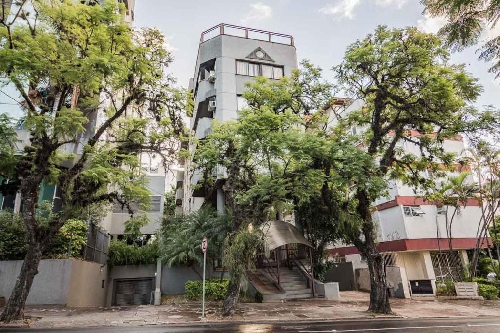 Un edificio alto y blanco con árboles delante. en Positano by My Way, en Porto Alegre