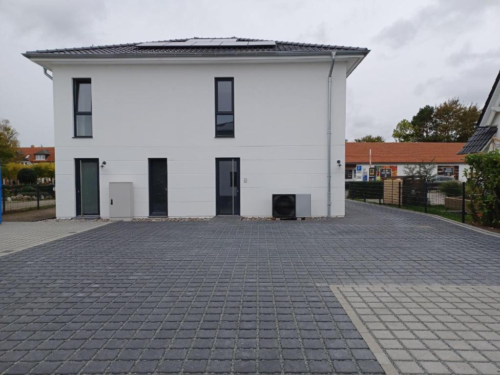 ein weißes Gebäude mit schwarzen Türen auf einer steinernen Einfahrt in der Unterkunft Boddenhörn 04 in Zingst