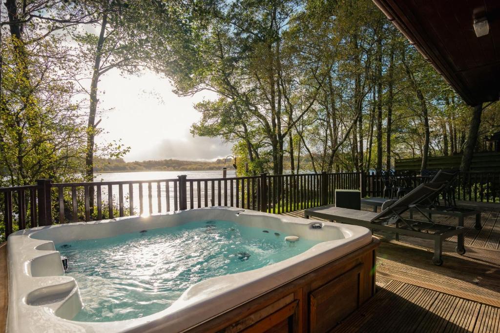 a jacuzzi tub sitting on a deck next to a lake at Heron Lodge with Hot-tub in Carlisle