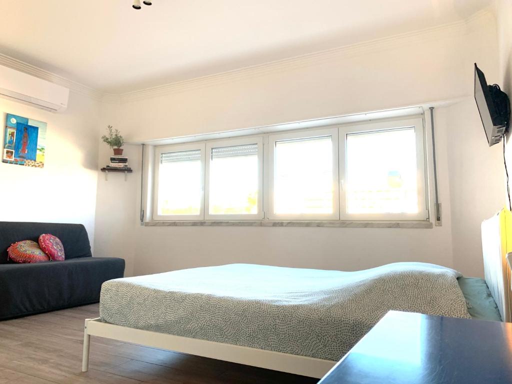 a bedroom with a bed and a couch and two windows at [MIRazul] Lovely condo 4 minutes walk to the beach in Costa da Caparica