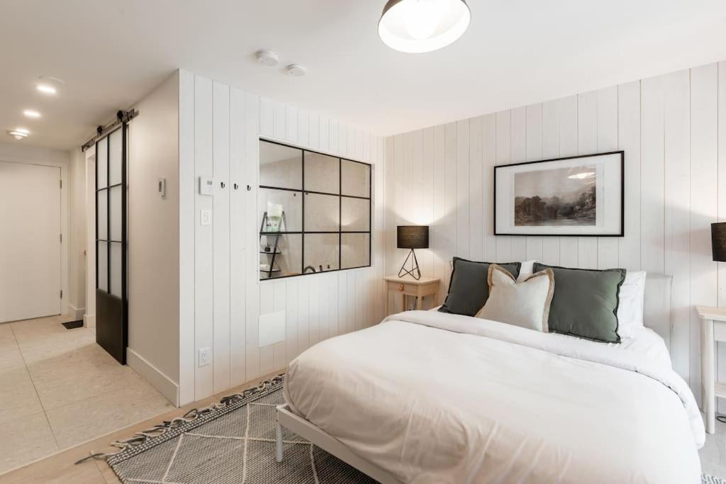 a white bedroom with a large bed and a hallway at Luxurious & Modern Tremblant Loft Pool&Spa Access in Mont-Tremblant