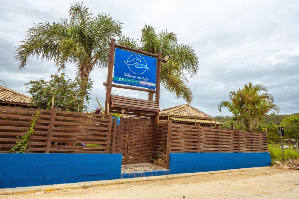 een bord voor een hek met palmbomen bij Pousada Refúgio do Rosa in Praia do Rosa