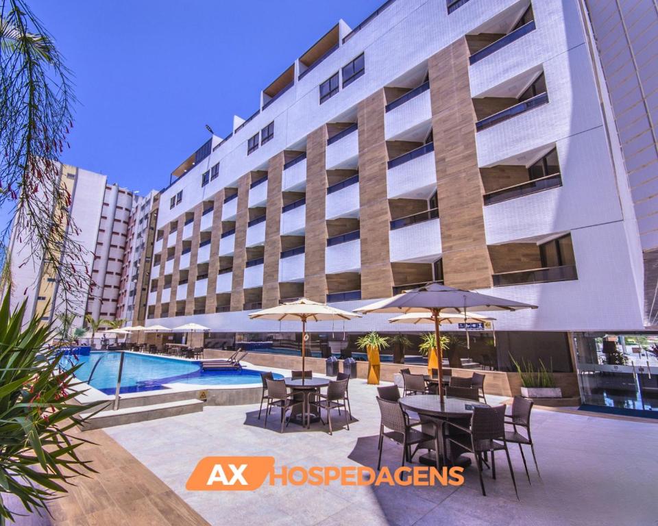 un hotel con mesas y sombrillas junto a una piscina en AX Gold Suítes, en João Pessoa