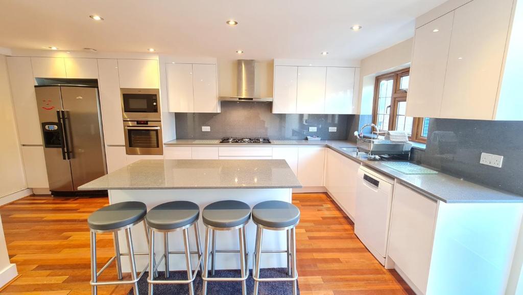 una cocina con armarios blancos y taburetes de bar en Luxury London House Sleeps x 16, Free Parking, Free Wifi, Garden Patio, Close to tube line easy access to Central London, en Ilford