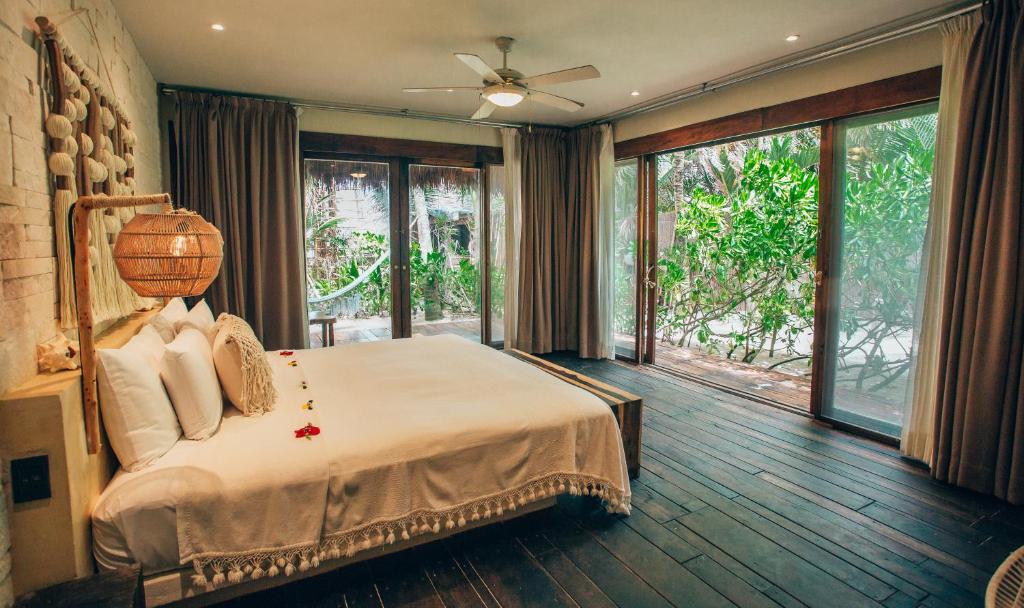 a bedroom with a bed with a ceiling fan and windows at Orchid House Tulum Beach in Tulum
